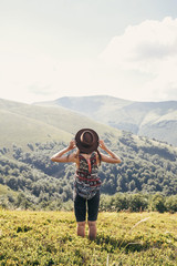 stylish traveler girl in hat looking at sunny mountains. summer vacation. travel and wanderlust concept. space for text. back view. woman traveling. amazing atmospheric moment