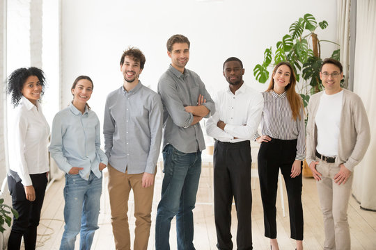Young happy multiracial professionals or company staff looking at camera smiling, multi-ethnic group of diverse business people standing together, employees posing in office, successful team portrait