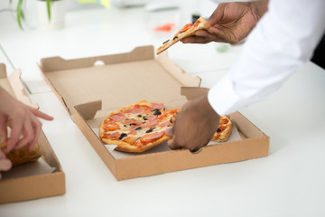 Hands of diiverse black and white people taking pizza slices from boxes on table, employees eat office lunch meal, friends celebrate party enjoy italian food, delivery service concept, close up view