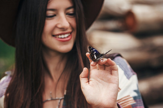 beautiful butterfly on girl hand. stylish hipster,happy woman in hat holding apatura iris  on fingers in forest in mountains. travel and wanderlust concept. space for text. amazing moment