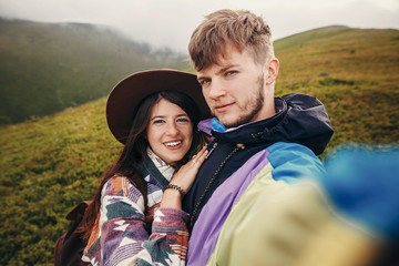 happy hipster couple making selfie on top of sunny mountains. summer vacation. space for text. atmospheric moment. travel and wanderlust concept. stylish man and woman traveling.