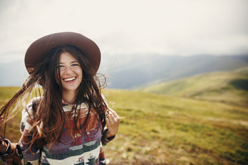 happy traveler hipster girl with windy hair  smiling, standing on top of sunny mountains. space for...