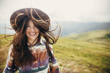 happy traveler hipster girl with windy hair  smiling, standing on top of sunny mountains. space for text. stylish woman in hat. atmospheric moment. travel and wanderlust. space for text