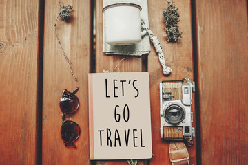 let's go travel text on notebook, wanderlust concept. map with sunglasses, photo camera, mug, notebook on wooden background, top view. stylish traveler hipster set flat lay