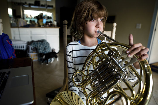 Girl practicing French horn while sitting on chair at home