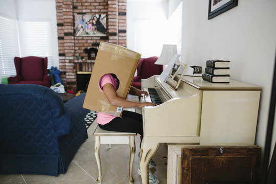 Side view of girl in cardboard box playing piano while sitting at home