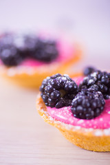 Closeup tartlets filled with pink berry cream and decorated with blackberries and powdered sugar