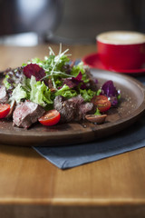 Salad with grelled beef on wooden plate