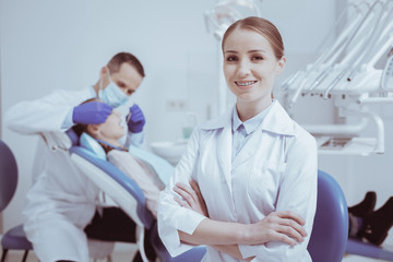 Ready for work. Inspired glad female dental assistant crossing arms and smiling to camera