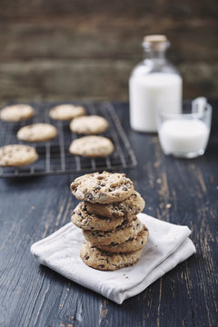 Stack of chocolate chip cookies with milk in background on wooden table