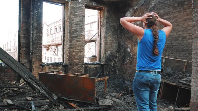 Sad man holds his head by hands and cry in burnt out house after disaster. Loss and despair concept