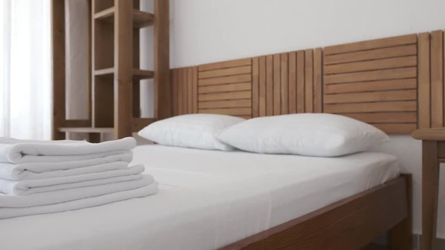 A set of white towels and blanket is lying on a comfortable bed in a hotel room with white curtains