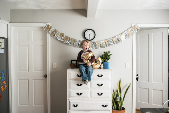 Birthday Boy With Number Balloon Sitting On Cabinet At Home