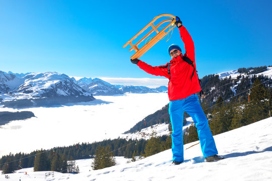 Young attractive man ready to go sledding in Swiss Alps during winter vacation