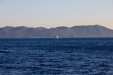 Widok z lądu na spokojnych wodach Morza Śródziemnego w Chorwacji. Na horyzoncie prom wracający...