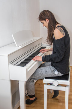 Junge Frau spielt zuhause Klavier, schulterfreies Oberteil, Tattoos