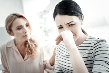 Im stuck. Disappointed unhappy tired woman sitting o the sofa touching her nose and crying.