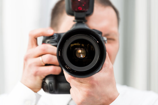 One young wedding photographer, ring, in dress shirt standing with camera, external flash, taking pictures macro closeup of lens, reflection