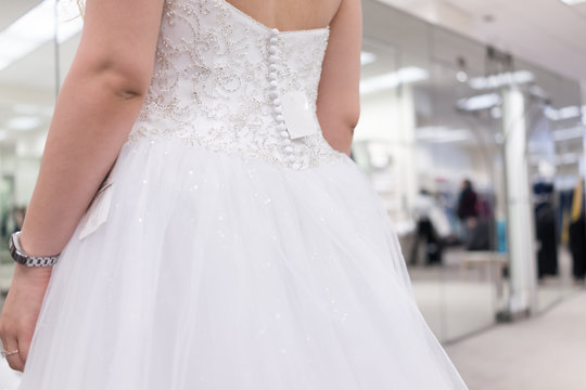 Closeup back of young woman trying on zipper zipped button wedding dress in boutique discount store with shiny tulle, price tag, engagement ring, fitness watch