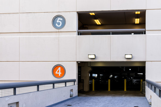 Retail department store mall parking garage with colorful color coded numbers for story level, cars, bridge passage to high building