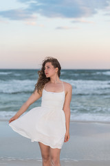 Fototapeta na wymiar Young woman in white dress on beach sunset in Florida panhandle with wind, ocean waves, side profile looking away
