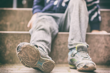 Alte kaputte Schuhe eines kleinen Jungen als Symbol für Kinderarmut