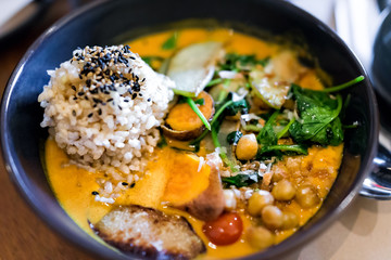 Closeup of Indian meal lunch or dinner dish in traditional Asian restaurant or cafe with vegetable sweet potato orange curry, brown rice, green cilantro parsley garnish, chickpeas, sesame seeds