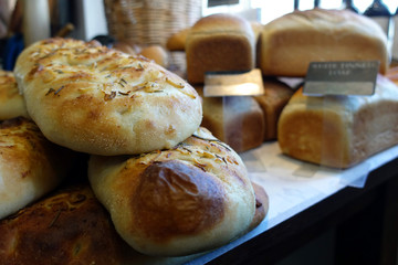 Shallow focus close up of rosemary and garlic focaccia bread, with other loaves in blurred background