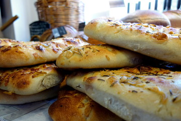 Shallow focus close up of rosemary and garlic focaccia bread, with other loaves in blurred background
