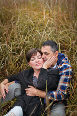 Loving attractive middle-aged couple looking tenderly at each other in autumn grass