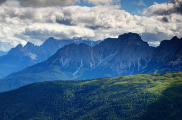 Forests, meadows in afternoon sunlight with jagged ridges in glowing blue mist and white cumulus clouds, Ciastelin and Aiarnola peaks Marmarole and Sesto Dolomiti Veneto Belluno Northern Italy Europe
