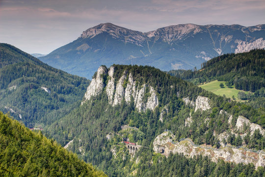 Austrian freight train on Semmering railway goes through Polleros tunnel in Polleroswand and Krausel Klause viaduct with Heukuppe peak in background, Rax Schneeberg Northern Limestone Alps Europe