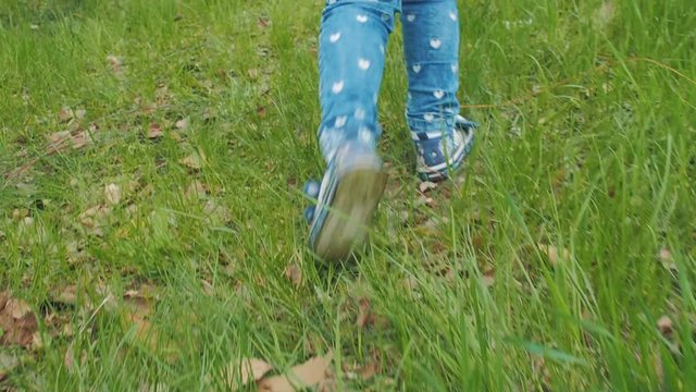 Legs of a child walking on green grass.