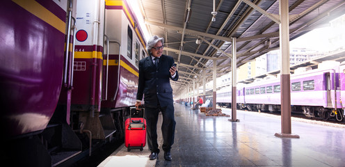 Asian business man looking at mobile phone when walks with suitcase in Train Station