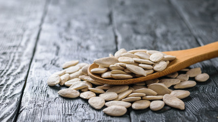 A bunch of pumpkin seeds and spoon on a dark rustic table.
