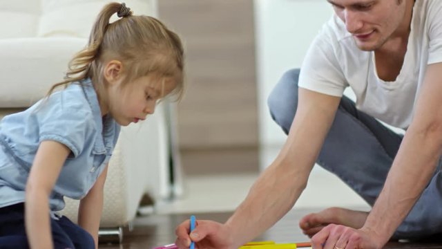Tilt down of adorable little girl and cheerful father sitting on floor and drawing with colored felt tip pencils