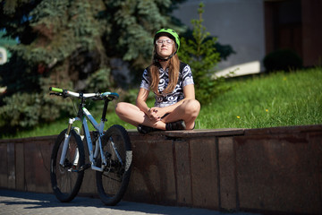 Fototapeta na wymiar Female cyclist in professional cycling clothing and helmet sitting on street edging near bike, enjoying sun with eyes closed. Relaxation after hard training, sportsman taking rest. Healthy lifestyle