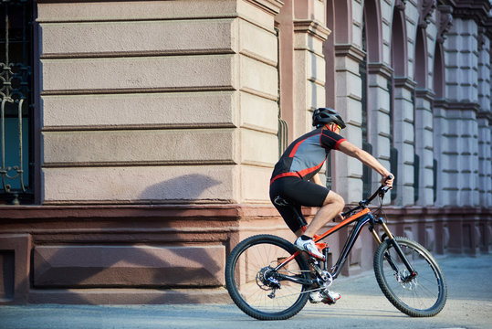Professional cyclist in cycling garment and protective gear riding bicycle in city center rushing and passing buildings. Sportsman training, exercising outdoors. Concept of healthy lifestyle
