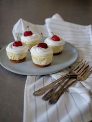 homemade personal cheesecakes with cherries and cream topping, on top of a ceramic plate
