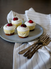 homemade personal cheesecakes with cherries and cream topping, on top of a ceramic plate