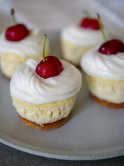 homemade personal cheesecakes with cherries and cream topping, on top of a ceramic plate