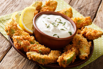 Delicious deep-fried avocado in bread crumbs with sauce and lemon close-up on a plate. horizontal