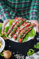 Woman hands holds plate with roasted baked eggplants slices with tomatoes, walnuts dressing, salad leaves and vegan sunflower seeds mayonnaise. Raw vegan vegetarian healthy food. Vegan lunch or dinner