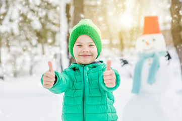 Smiling boy with snowman on background showing thumbs up