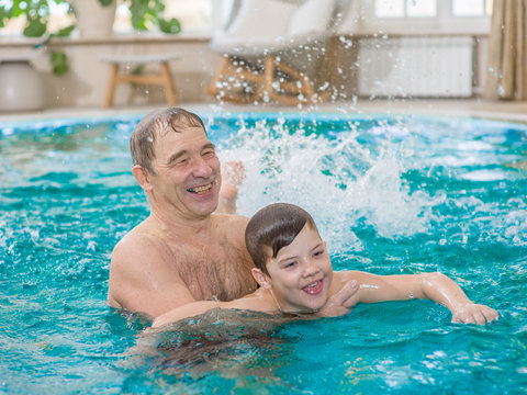 Happy elderly man teaches to swim a boy in the pool