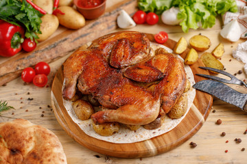 Juicy tobacco chicken with potato garnish on a round wooden board.