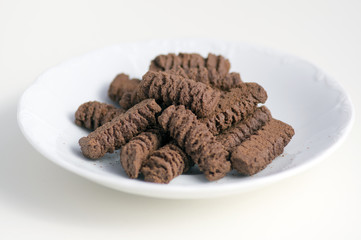 Dark brown cocoa tea biscuits on white plate, tasty unhealthy sweets