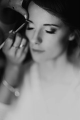 beautiful stylish bride with red hair getting make up done by professional stylist, morning preparation. wedding getting ready, space for text. expert beauty artist. black white photo