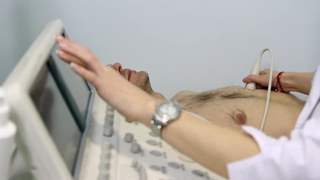 Female doctor examines patient's heart with modern ultrasound echocardiography equipment in hospital operating room.
