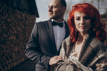stylish groom and happy bride in blanket hugging in light on background of wooden firewood wall. rustic wedding in barn concept, space for text. newlyweds couple embracing, romantic moment © sonyachny